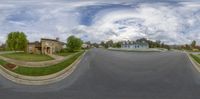 a fish eye photo looking down a street of a residential area with houses and clouds in the background