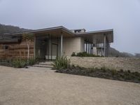 the front of a home with a very low roof and concrete walls and plants in front of it