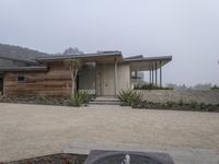 the front of a home with a very low roof and concrete walls and plants in front of it