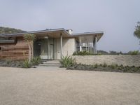 the front of a home with a very low roof and concrete walls and plants in front of it