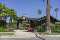 a red car parked in front of a house with tall palm trees near it, and a driveway