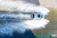 an suv drives through the water on its way to shore with large waves coming from behind