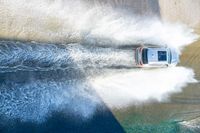 an suv drives through the water on its way to shore with large waves coming from behind