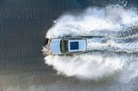 white speedboat traveling through a body of water splashing with water behind it with a sky background