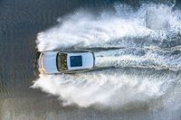 white speedboat traveling through a body of water splashing with water behind it with a sky background