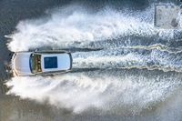 white speedboat traveling through a body of water splashing with water behind it with a sky background