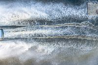 white speedboat traveling through a body of water splashing with water behind it with a sky background