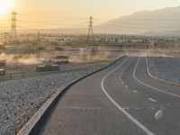 a highway with dirt running alongside it and buildings along the edge at sunset with mountains in the background