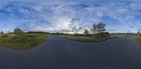 a wide angle lens picture showing a road with grass on either side and a field with trees