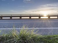 a highway next to some water and some grass with the sun shining above it and a sea