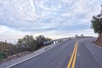 a curved road winds through a scenic area under a cloudy sky at dusk with traffic