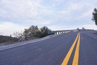 a curved road winds through a scenic area under a cloudy sky at dusk with traffic