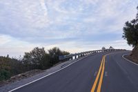 a curved road winds through a scenic area under a cloudy sky at dusk with traffic