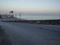 a stop light sits on a paved street near the beach and water line at dusk