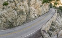 a motorcycle rides along a curve on the road by the mountain cliff side, while it is surrounded by trees