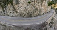 a motorcycle rides along a curve on the road by the mountain cliff side, while it is surrounded by trees