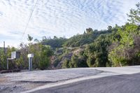 a street view shows a roadway and trees on the hill near a gate on an angle