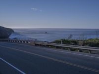 an empty highway near a large body of water with an ocean and cliffs in the background