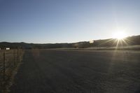 the sun shines brightly on the road next to a fence and farm animals on a ranch