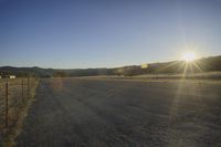 the sun shines brightly on the road next to a fence and farm animals on a ranch