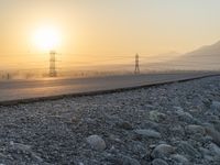 the sun is rising over a highway and hills with power lines going through it on the road