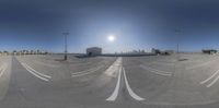 an empty parking lot with sun going down and buildings in the distance at the back