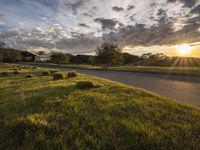 a sun setting over a golf course and a house with a lot of grass in front