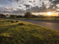 a sun setting over a golf course and a house with a lot of grass in front