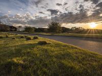 a sun setting over a golf course and a house with a lot of grass in front