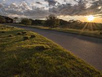 a sun setting over a golf course and a house with a lot of grass in front