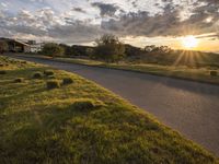 a sun setting over a golf course and a house with a lot of grass in front