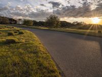 a sun setting over a golf course and a house with a lot of grass in front