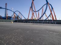 a roller coaster sits in front of a building and is blue with orange accents and has two red steel bars on the sides of it