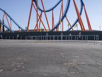 a roller coaster sits in front of a building and is blue with orange accents and has two red steel bars on the sides of it