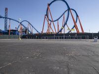 a roller coaster sits in front of a building and is blue with orange accents and has two red steel bars on the sides of it