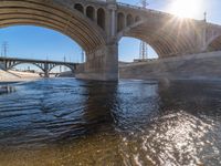 sunlight reflecting off the water and beneath an overpass with a bridge in it and several power lines