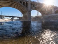 sunlight reflecting off the water and beneath an overpass with a bridge in it and several power lines