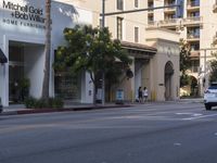 two people are crossing the street with traffic light on in front of him, where the buildings are tan and one is white