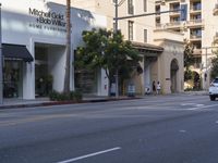 two people are crossing the street with traffic light on in front of him, where the buildings are tan and one is white