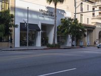 two people are crossing the street with traffic light on in front of him, where the buildings are tan and one is white