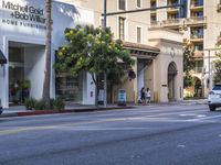 two people are crossing the street with traffic light on in front of him, where the buildings are tan and one is white