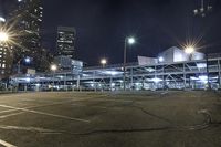 an empty lot next to a lot with parking spaces and tall buildings at night time