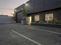 an empty parking lot with a black building in the back ground and white lines painted on the ground