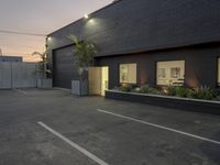 an empty parking lot with a black building in the back ground and white lines painted on the ground