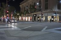 people are walking on the sidewalk near shops at night in front of the street light