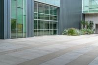 the concreteed walkway is lined with glass windows and a bench outside a building that is surrounded by greenery