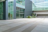 the concreteed walkway is lined with glass windows and a bench outside a building that is surrounded by greenery