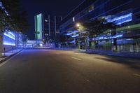 a city road at night with bright lights on both sides of it and green buildings in the background