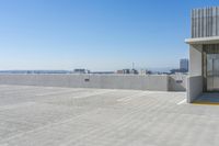 a building on the ground in front of a city skyline and the ocean view, showing its concrete facade