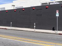 a wall is painted with red light lights next to a parking meter and sidewalk and two vehicles pass by